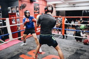 wo boxers engaged in a sparring match at KOS boxing ring, spectators watching with intensity.